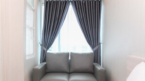 Ein modernes Zimmer mit einem grauen Sofa, einem kleinen Nachttisch und einem Fenster mit dunklen Vorhängen.
