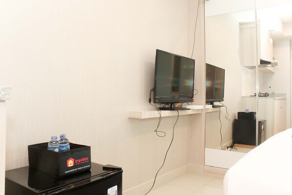 A hotel room with a television on a stand, a minibar with a travelio label, and a mirror reflecting the room.