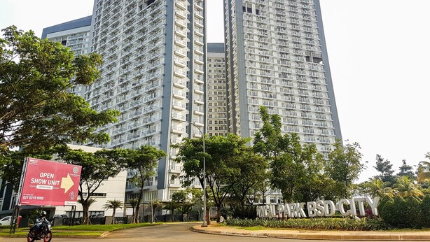 A high-rise building with multiple balconies and a sign indicating a show unit. - Compact and Modern Studio Room at Casa De Parco Apartment (Pagedangan)