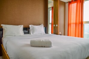 Una habitación de hotel con una cama grande, ropa de cama blanca y una toalla blanca enrollada sobre la cama.