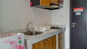 A compact kitchen with a stainless steel sink, a built-in stove, and wooden cabinets. - Compact and Modern Studio Room at Casa De Parco Apartment (Pagedangan)