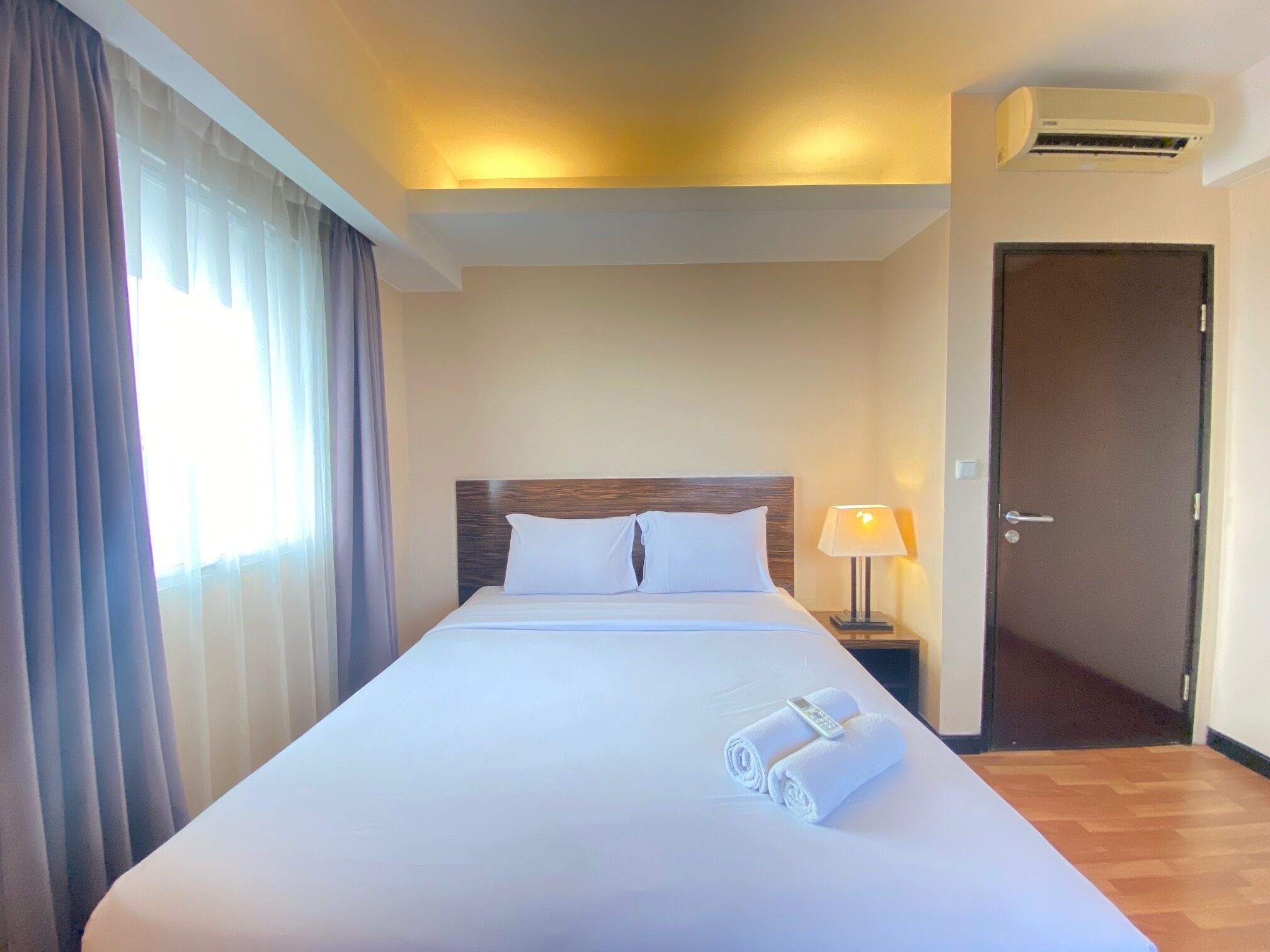 Une chambre d’hôtel avec un grand lit, une table de chevet avec une lampe, un appareil de climatisation et une porte.