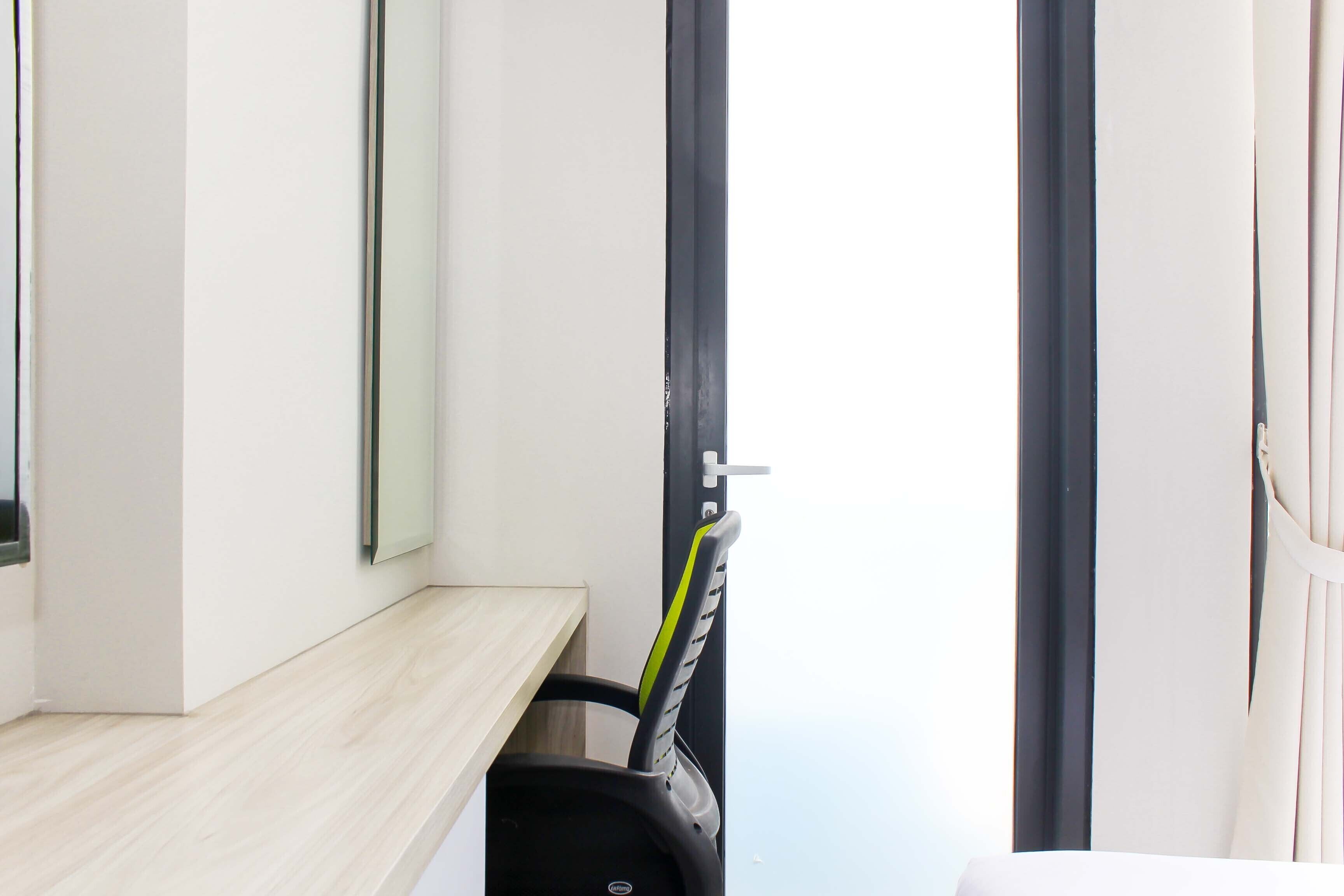 Une chambre moderne avec un bureau en bois, une chaise noire avec une bande verte et une fenêtre à cadre noir.