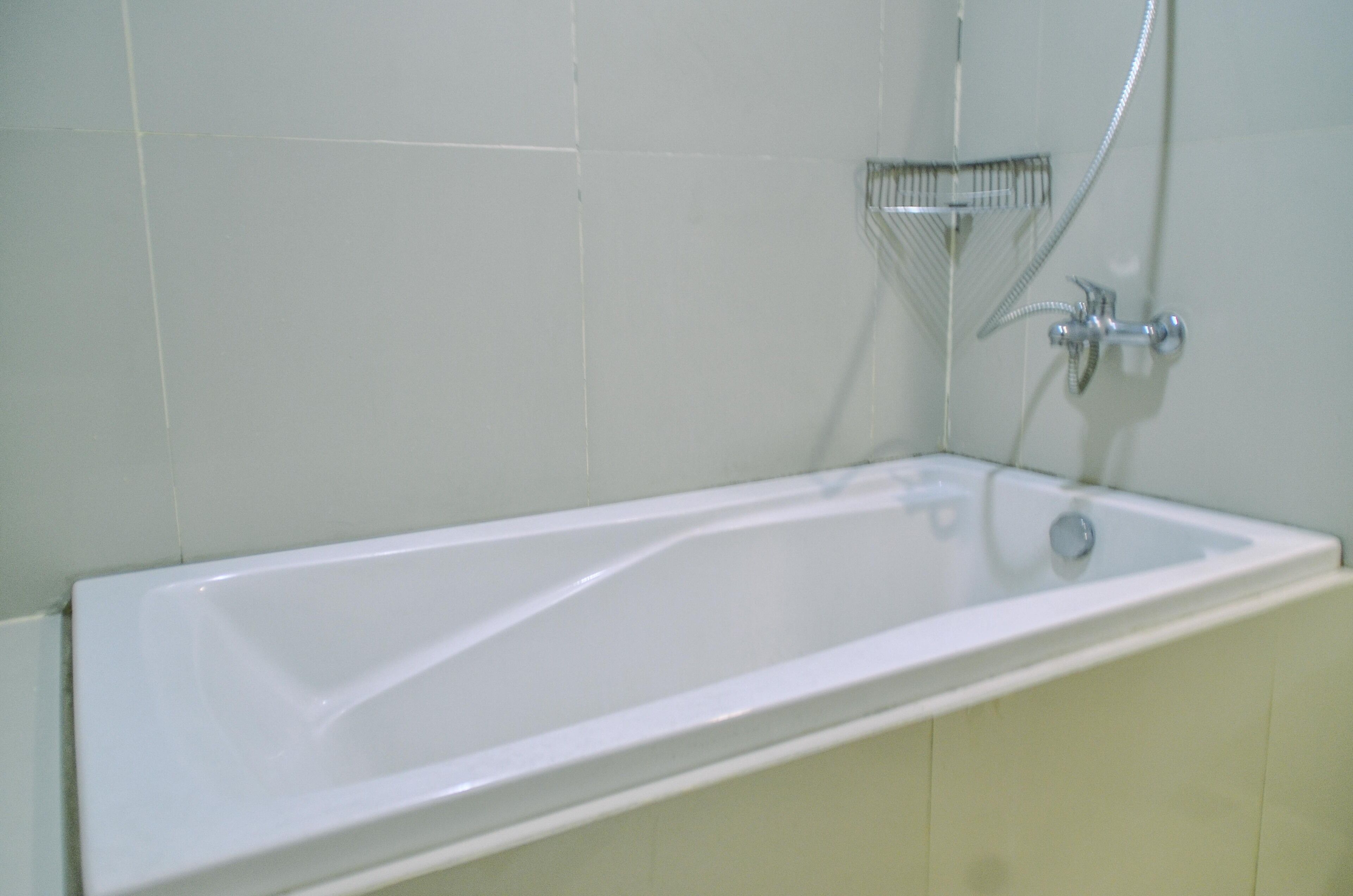 A white bathtub with a shower head and faucet, set against a tiled wall.