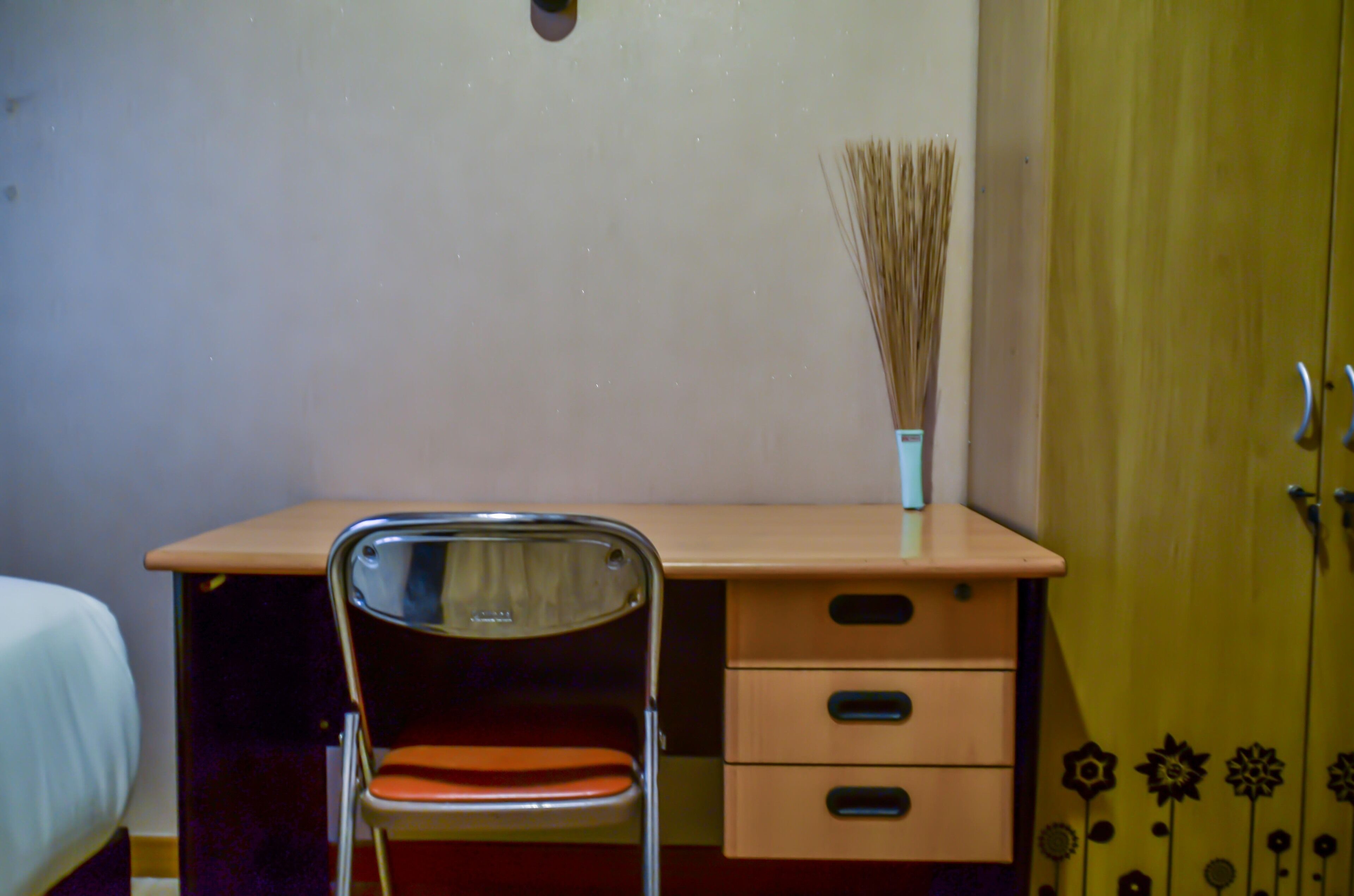 A room with a wooden desk, a chair, a bed, and a wardrobe.