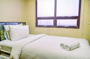 Hotellihuone, jossa on sänky, tyynyjä, ikkuna ja sängyllä rullalle taitettu pyyhe.