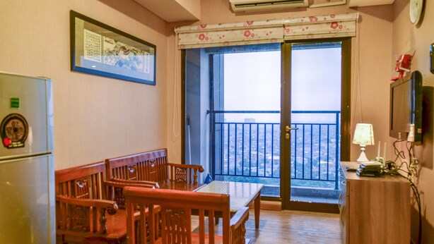 Une chambre avec un balcon, une table à manger avec des chaises, un réfrigérateur et une lampe.