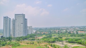 Een hoog appartementencomplex met meerdere verdiepingen en balkons, omringd door groene ruimtes en een verre zicht op een stad.