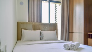 Een net opgemaakt bed met witte lakens en kussens, een houten hoofdbord en een raam met gordijnen.