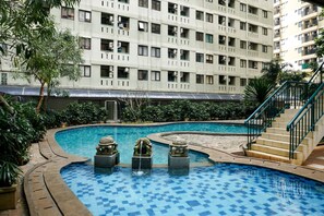 A swimming pool with a checkered pattern, surrounded by greenery and a multi-story building with balconies. - Homey and Simply Studio Room at Kebagusan City Apartment (Jakarta)
