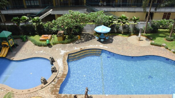 A swimming pool with a curved design, surrounded by a stone pathway and greenery. - Comfort Living 2BR at Kebagusan City Apartment (Jakarta)