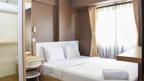 A neatly arranged hotel room with a bed, a desk, a chair, and a window with curtains. - Comfort Living 2BR at Kebagusan City Apartment (Jakarta)