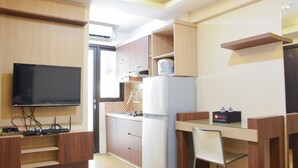A compact kitchen with a built-in TV, a refrigerator, and a dining area with a chair. - Comfort Living 2BR at Kebagusan City Apartment (Jakarta)