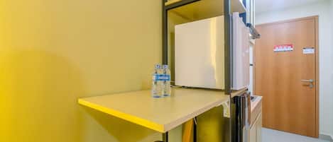 Habitación de hotel con kitchenette, una mesa pequeña y una botella de agua, y una puerta con un cartel.