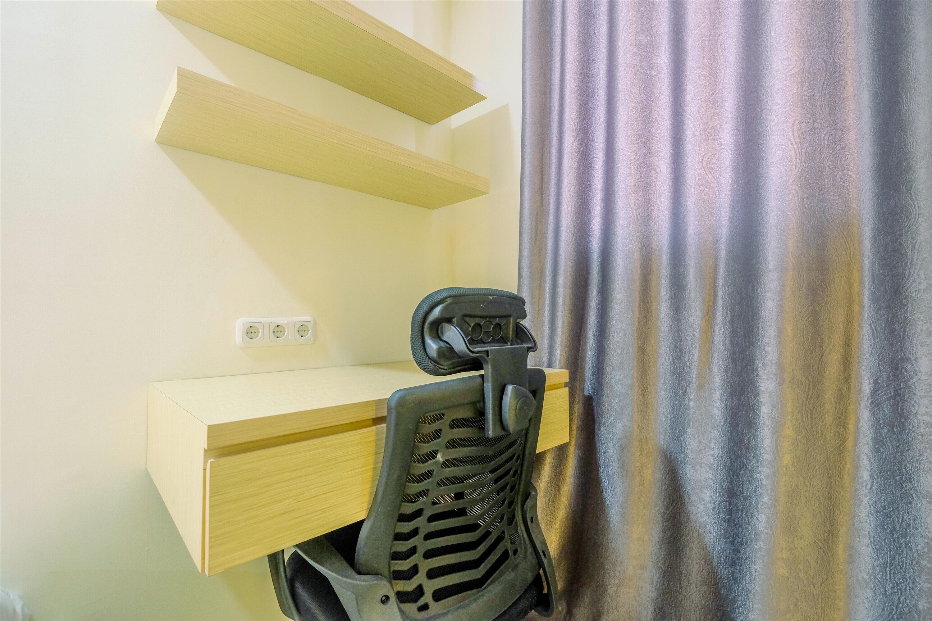 Un bureau avec une chaise, une prise de courant et un rideau.