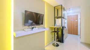 A modern hallway with a mounted TV, a white shelf with electronic devices, a bar stool, and a refrigerator.