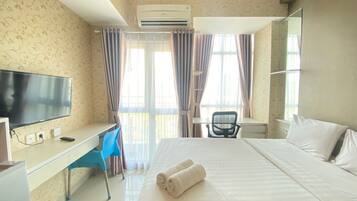A hotel room with a bed, a desk, a chair, a TV, and an air conditioning unit.