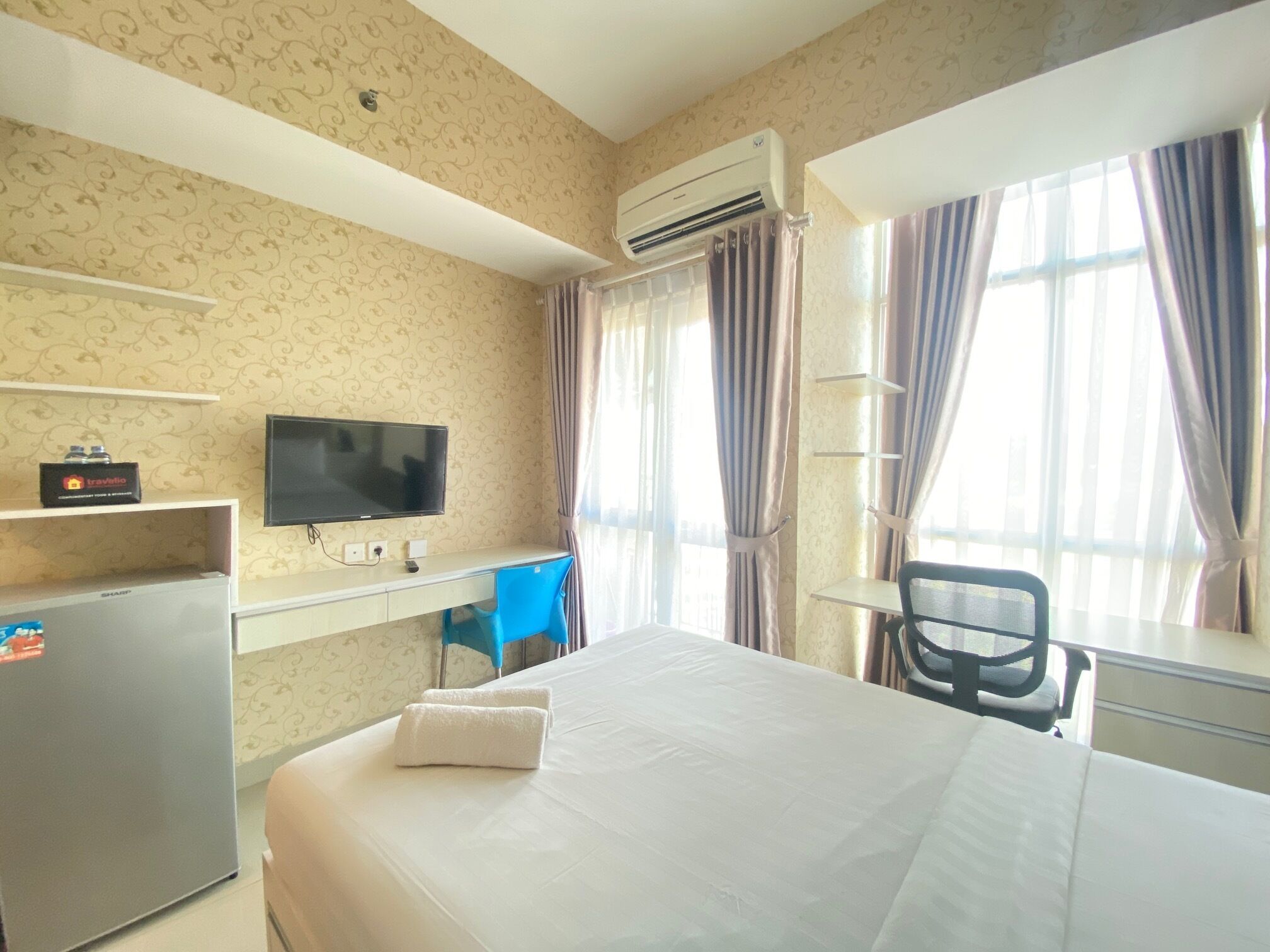 A hotel room with a bed, a desk with a computer, a TV, and an air conditioning unit.