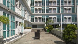 Un edificio de varios pisos con balcones, un patio con plantas en macetas y asientos al aire libre.