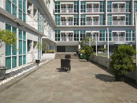 Un edificio de varios pisos con balcones, un patio con plantas en macetas y asientos al aire libre.