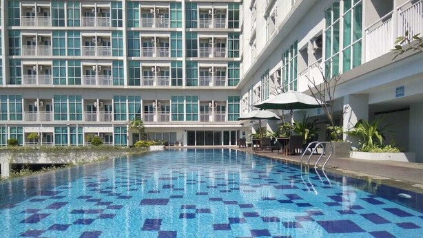 Una piscina con diseño de cuadros, rodeada por un edificio con balcones y una zona de estar techada.