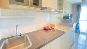 Una cocina moderna con un lavamanos de acero inoxidable, una placa de inducción roja y armarios blancos.