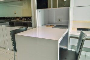 A modern kitchen with white countertops, a built-in stove, and a small island with a cutting board.