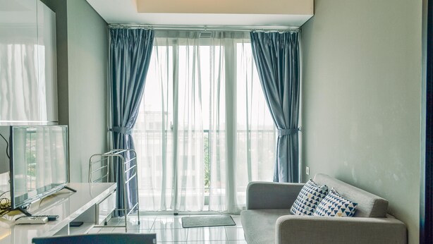 Uma sala de estar moderna com sofá, televisão e varanda com cortinas.