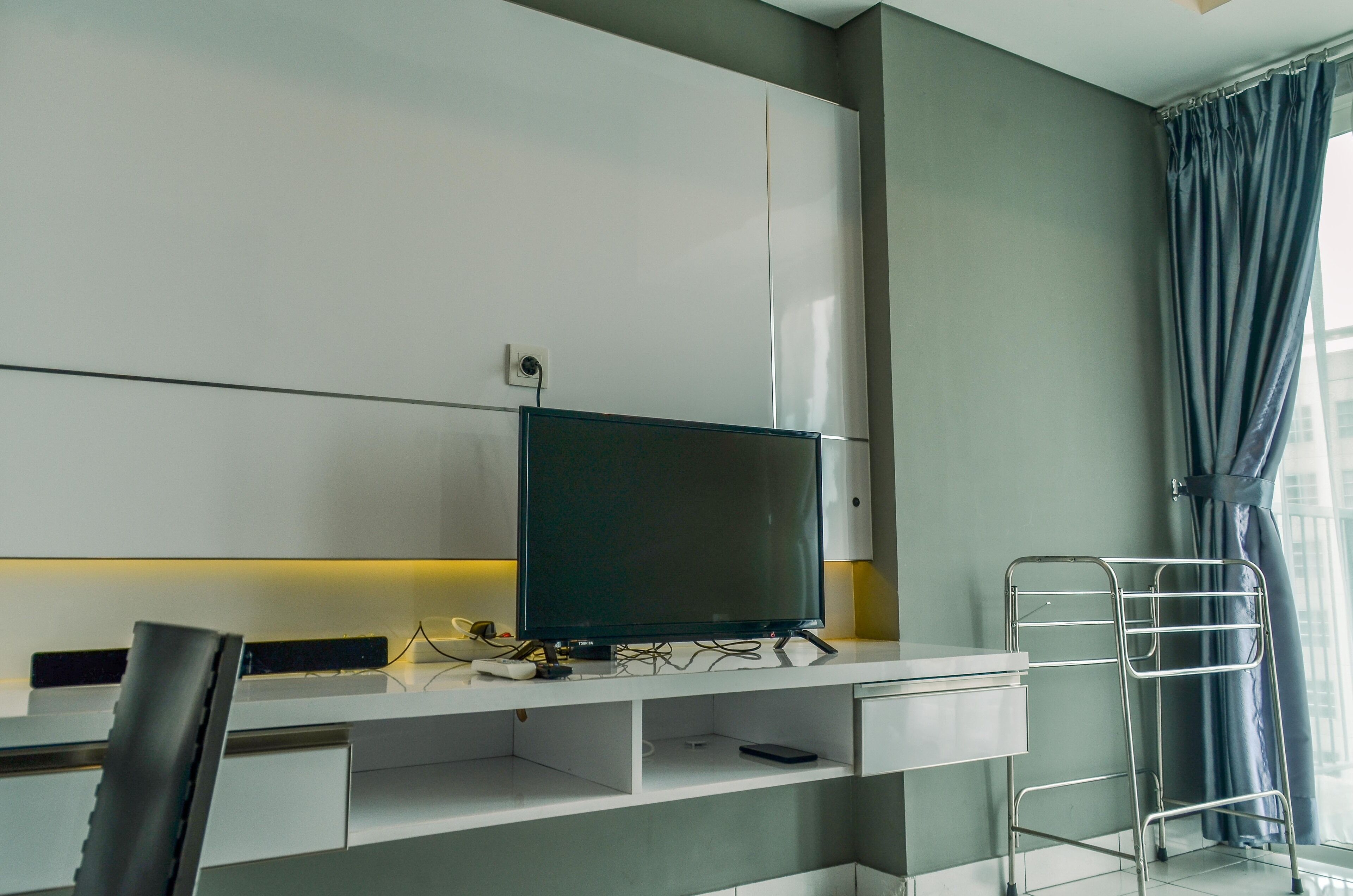 Una habitación de hotel moderna con escritorio, televisor de pantalla plana, una silla y un perchero metálico.
