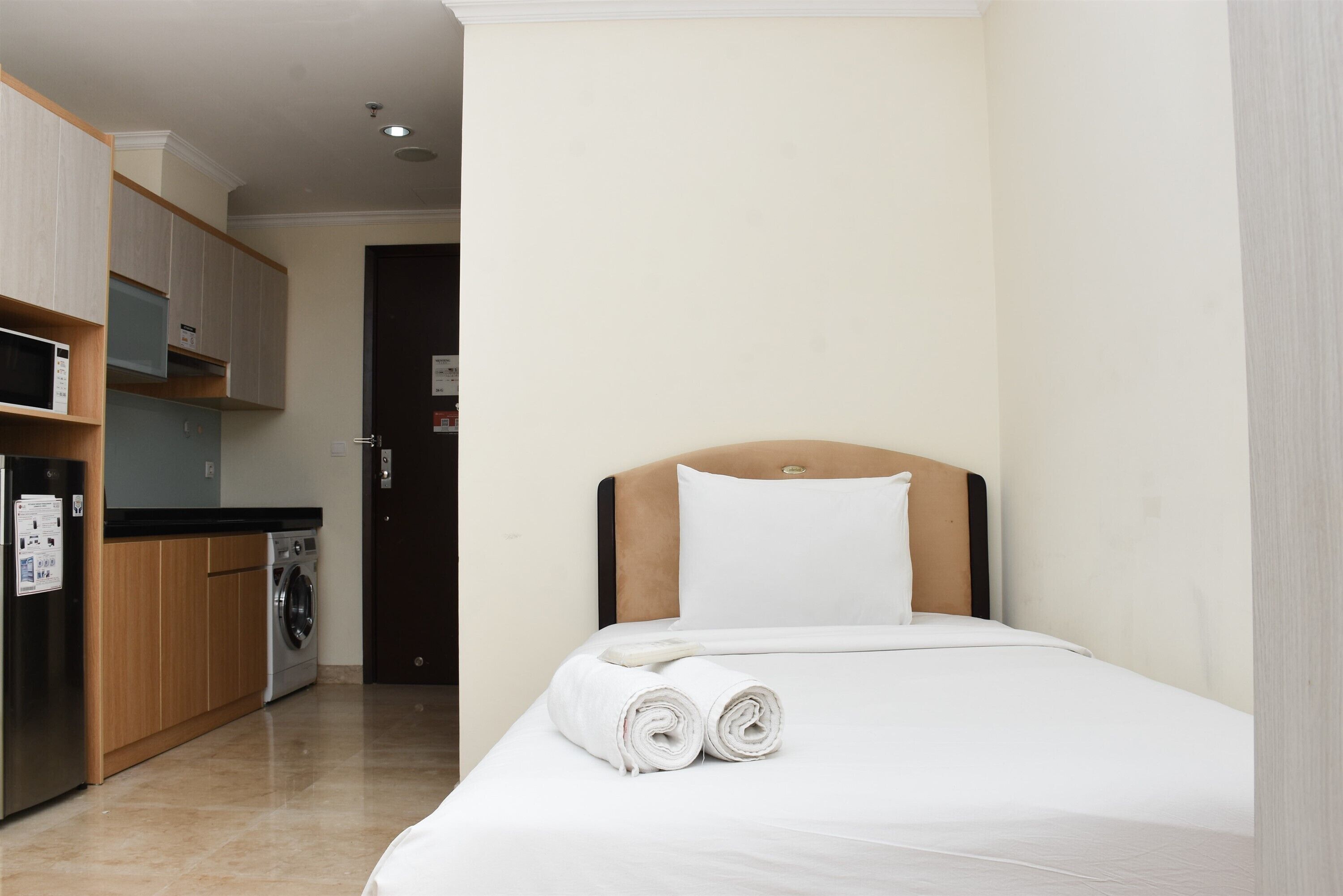 A hotel room with a bed, a small kitchenette, and a door leading to another room.