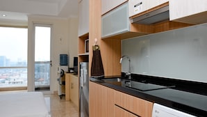 A modern kitchen with wooden cabinets, a black countertop, and a stainless steel refrigerator. - Stunning and Comfy Studio at Menteng Park Apartment (Jakarta)