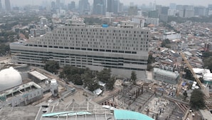 A large, multi-story building with a grid-like facade, surrounded by other buildings and construction sites. - Stunning and Comfy Studio at Menteng Park Apartment (Jakarta)