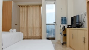 A hotel room with a bed, a TV, a water dispenser, and a view of the city through the window. - Stunning and Comfy Studio at Menteng Park Apartment (Jakarta)
