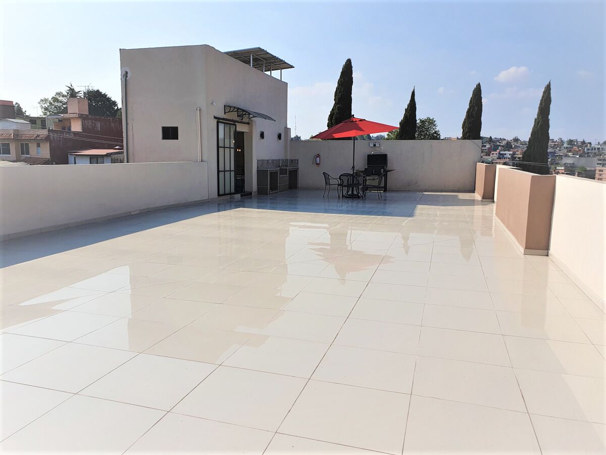 A rooftop terrace with a tiled floor, a grill, and a red umbrella.