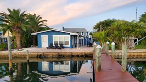 Une propriété située au bord de l’eau, avec un bâtiment bleu, un quai et des palmiers.