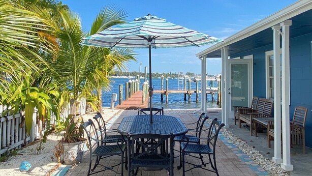Une terrasse avec une table et des chaises, un parasol à rayures et une vue sur l’eau et les quais.