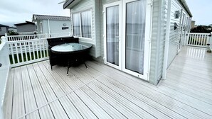 A covered outdoor area with a hot tub, a white fence, and a building with a sliding glass door. - 63 Bude Perran Paradise (Newquay)