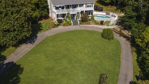 Vue aérienne d’une maison à deux étages, dotée d’une grande pelouse, d’une piscine et d’une allée.