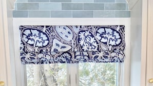 Eine Küche mit Spüle, einem Fenster mit gemustertem Vorhang und zwei Blumentöpfen auf der Arbeitsfläche.