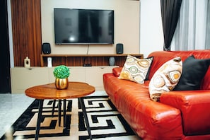 Un salon moderne avec un canapé en cuir rouge, une table basse ronde en bois, une petite plante verte et un tapis à motifs noir et blanc.