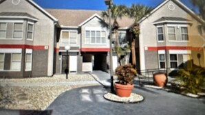 A two-story building with a red awning and a small garden area with potted plants. - Best Apartment in Kissimmee ! 1 Free dinner ! (Kissimmee)