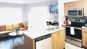 A compact kitchen with a dishwasher, microwave, and stove. There is a dining area with a table and chairs, and a sofa with cushions. - Best Apartment in Kissimmee ! 1 Free dinner ! (Kissimmee)