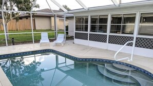 Une piscine à bord incurvé, un patio couvert et une vue sur une maison dotée d’une cour clôturée.