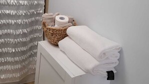 Ein Badezimmer mit weißem Handtuchhalter, gefalteten Handtüchern, einem Korb mit Pflegeprodukten und einem Toilettenpapierhalter.