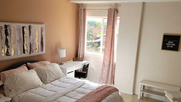 Ein Schlafzimmer mit Bett, Nachttisch, Lampe und Blick ins Freie.