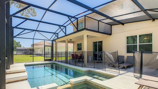 Una piscina con cerramiento de vidrio, mobiliario exterior y vistas de los alrededores.