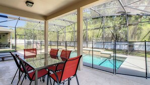 Un espacio al aire libre cubierto con una mesa de vidrio y sillas rojas, con vista a una piscina.
