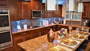 A kitchen with granite countertops, wooden cabinets, stainless steel appliances, and a breakfast bar set for four. - Exquisite Destination Villas... Crystal location (Kissimmee)