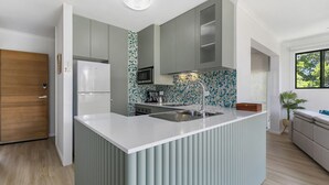 A modern kitchen with grey cabinets, a white countertop, and a blue mosaic backsplash.