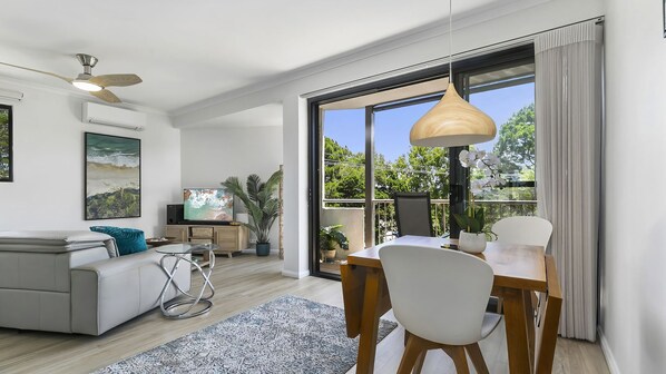 Relax in this stylish living room with a sofa, coffee table, dining table, and TV, surrounded by lush views.